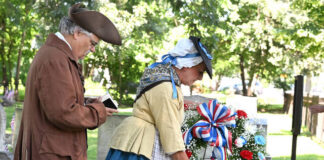 
			
				                                Sherry Emershaw, portraying Amy Harding, and Mark Kahn, portraying Rev. Joshua Entwhistle, as they play a wreath at the grave of Benjamin and Stuckley Harding during a ceremony in 2025, who was killed by the Indians on June, 30, 1778.
                                 Tony Callaio file photo | For Sunday Dispatch

			
		